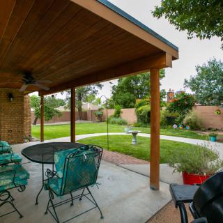 A covered patio with outdoor seating overlooks a well-maintained backyard garden.