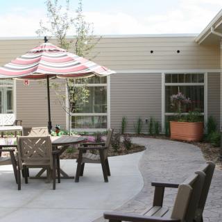 A cozy outdoor patio area with chairs and a table under a striped umbrella, set next to a garden path.