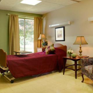 A cozy hospital room with a bed, sofa, and natural light from the window.