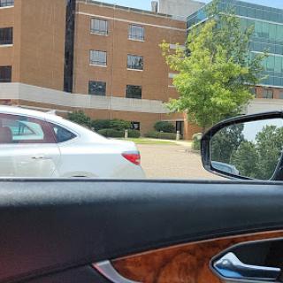 A view from inside a car, showing a white vehicle parked next to a building with large windows.