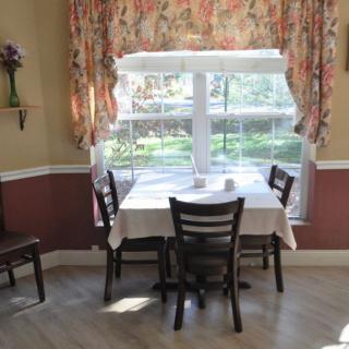 A cozy dining area with a table and chairs by a sunlit window with floral curtains.
