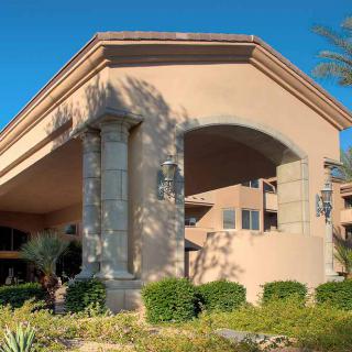 A sunny view of a large residential building with an arched entrance and manicured landscape.