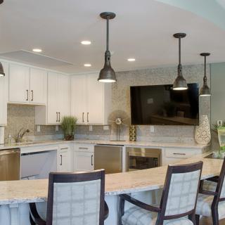 A modern kitchen interior featuring bar stools, pendant lighting, and a mounted television.