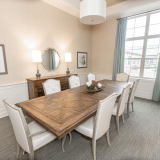A well-decorated dining room featuring a large wooden table with white chairs, ambient lighting, and a window with curtains.
