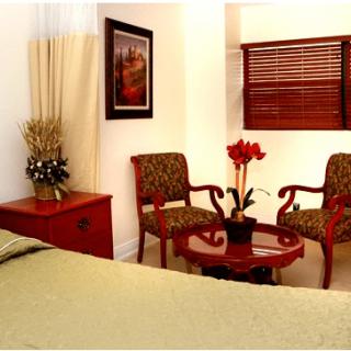 A cozy bedroom featuring a pair of upholstered chairs and a small round table, complemented by artwork and window blinds.