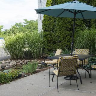 A cozy patio setup with a table, chairs, and an umbrella amidst lush garden greenery.