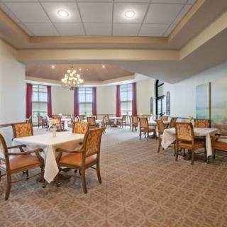 An elegant dining room with neatly arranged tables and chairs, featuring a chandelier and large windows.