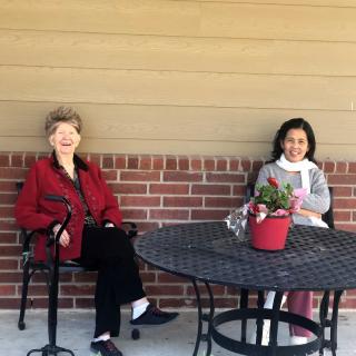 Two people sitting at a table outside, with a potted plant on the table.