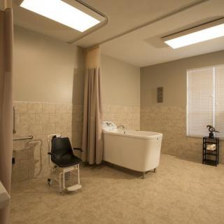 A spacious and accessible bathroom with a bathtub and medical chair, designed for use in healthcare facilities.