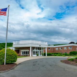 A view of a building entrance with an American flag in the foreground under a cloudy sky.