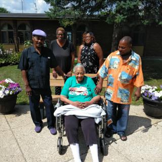 A joyful family gathering with a beloved senior member enjoying a sunny day outdoors.