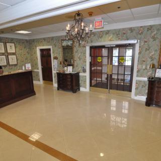 A well-lit lobby with a chandelier, featuring decorative wallpaper and floor tiles, leading to entrance doors.
