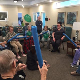 Elderly individuals participating in a group exercise session using foam noodles in a retirement home.