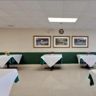 A neatly arranged dining area with tables covered in white tablecloths and adorned with decorative centerpieces, surrounded by wall art and a clock.