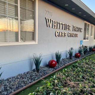 Exterior view of a care center building with landscaped plants and a sign reading 'Whittier Home Care Center'.