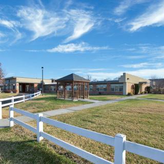 A scenic view of a building with a white fence and open grassy area under a blue sky with clouds.