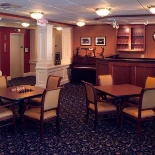 A cozy interior dining space with several tables and chairs, featuring a carpeted floor and a small bar area.