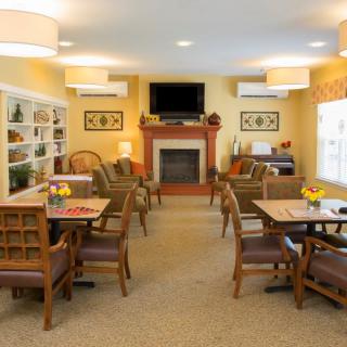 A cozy and well-furnished common living area with tables, chairs, a fireplace, and a television.