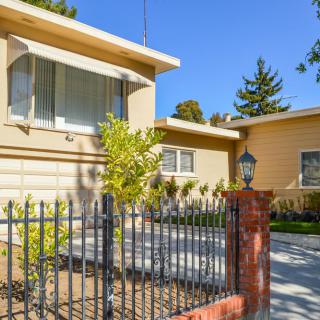 A suburban residential house with a driveway and front yard, surrounded by a fence.