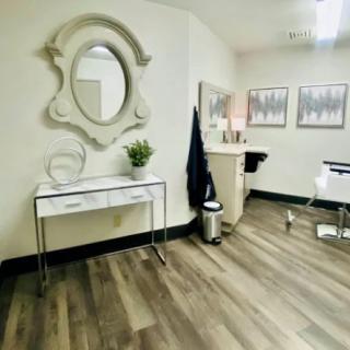 A modern interior space with minimalist decor, featuring a mirror, hardwood floors, and a barber chair.