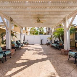 A spacious backyard patio featuring a pergola with outdoor seating and lush palm trees.