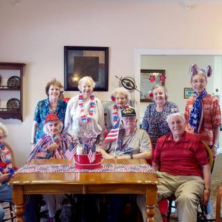 A group of elderly people dressed in patriotic attire, gathered around a table with an American flag centerpiece.