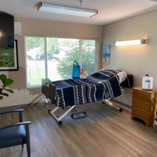 A well-lit hospital room featuring an adjustable bed, a chair, and natural light from the window.