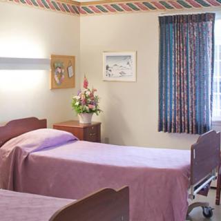 A hospital room with two neatly made beds and a small bedside table with flowers.