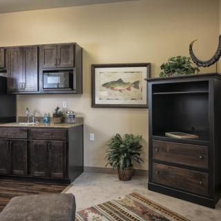 A modern kitchen interior featuring dark wooden cabinets, a small sink area, and decorative elements including artwork and a green plant.