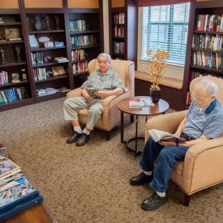 Two seniors reading books in a cozy library setting.