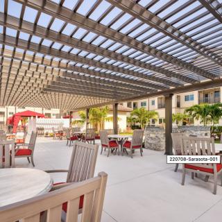 A modern outdoor patio area with wooden pergolas providing shade over tables and chairs.