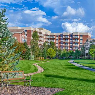 A scenic view of a landscaped park with benches, pathways, and a building in the background under a cloudy sky.