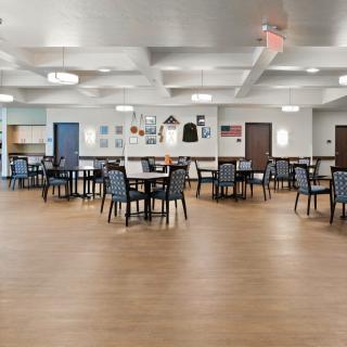 An empty dining area with neatly arranged tables and chairs, featuring wooden flooring and ceiling lights.