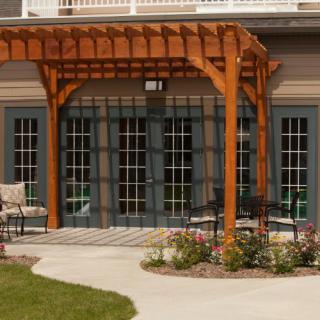 A wooden pergola with outdoor seating on a patio, surrounded by a landscaped garden.