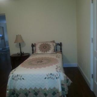 A minimalist bedroom with a single bed, quilt, and nightstand with a lamp.