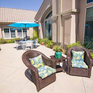 A sunny patio featuring wicker chairs with patterned cushions and a table with an umbrella.