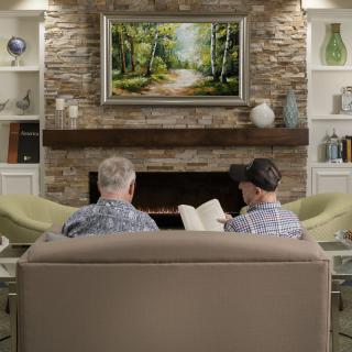 Two people sitting on a couch in a cozy living room with a fireplace and artwork.