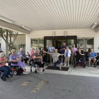 A group of people gathered outside a building, some sitting in wheelchairs.