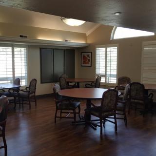 A well-lit dining room with multiple tables and chairs, featuring wooden flooring and large windows.