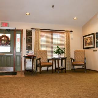A cozy lobby area with chairs and a small table, adorned with paintings and a window overlooking outside.