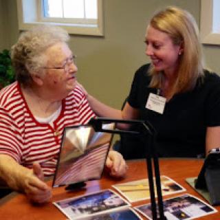 A heartwarming moment between a caregiver and an elderly woman, sharing memories through photos.