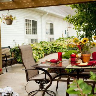 A cozy patio with a glass table and chairs, surrounded by lush garden foliage and vibrant flowers.