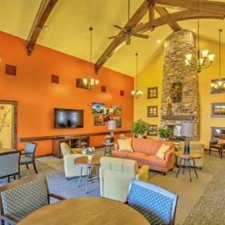 A cozy living room with an orange accent wall, high ceilings with wooden beams, a stone fireplace, and comfortable seating.