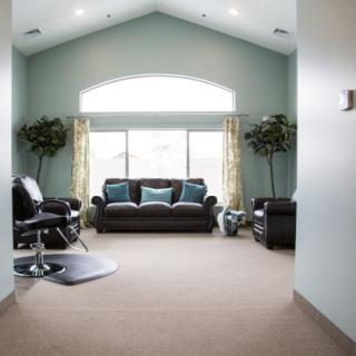 A bright and spacious living room with a sofa and armchairs, featuring large windows with curtains and decorative plants.