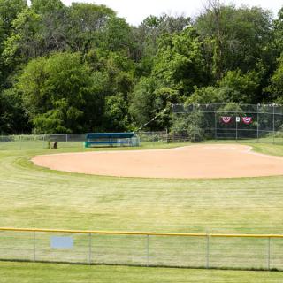 A baseball field surrounded by trees and a fence, with a bench in the background.
