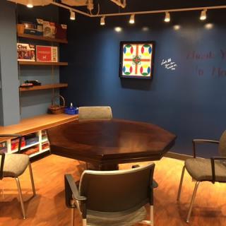 A cozy meeting room with a wooden table, modern chairs, and artwork on a blue wall.