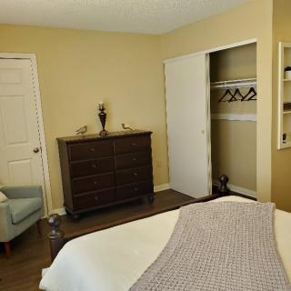 A cozy bedroom featuring a dresser, an open closet, and a comfortable chair in neutral tones.