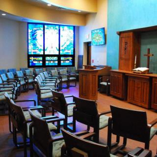 A peaceful chapel interior featuring rows of chairs, a stained glass window, and an altar.