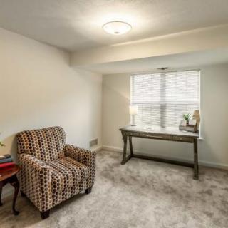 A cozy room with a patterned chair, desk, and window.
