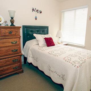 A cozy bedroom with a bed and wooden dresser next to a window.